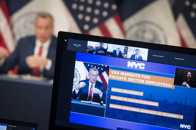 Mayor de Blasio is seen in the background with a monitor in the foreground that describes NYC's vaccine mandate for the private sector, which begins December 27th
